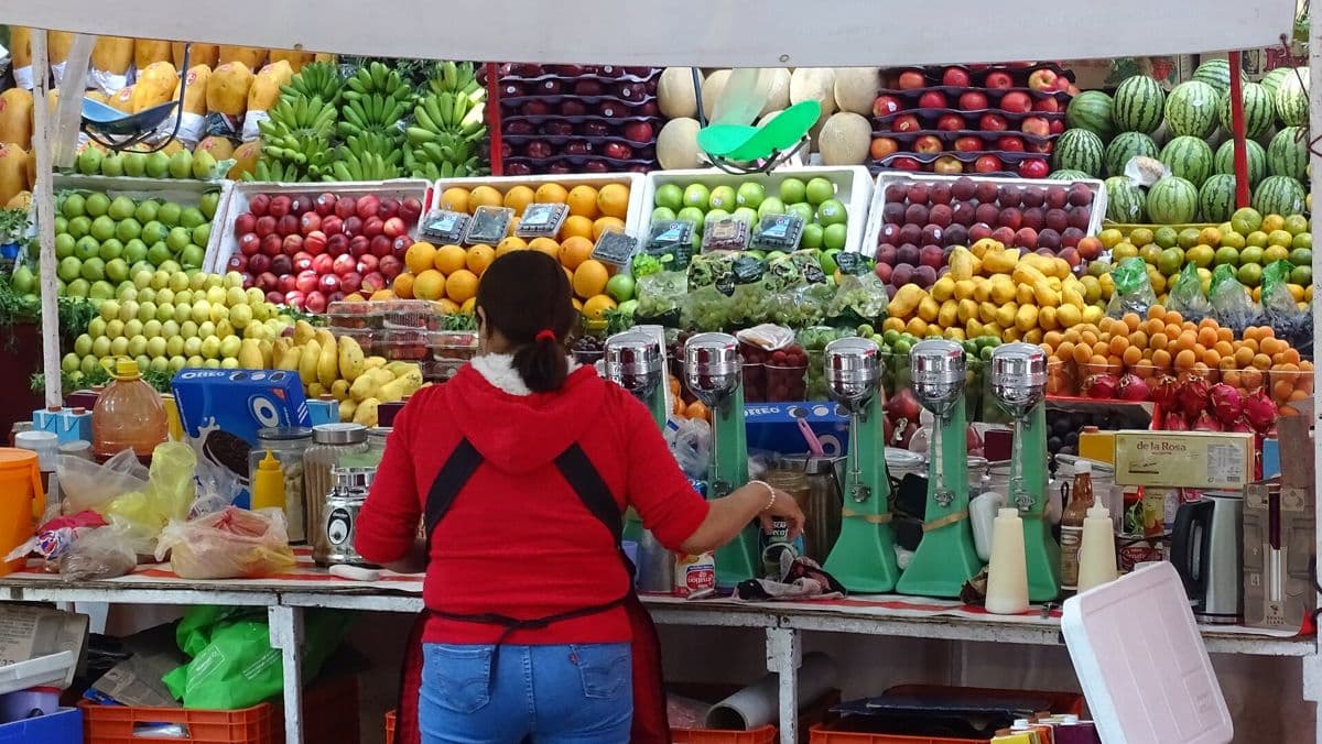 A woman tending a colourful fruit and vegetable stall at a market.